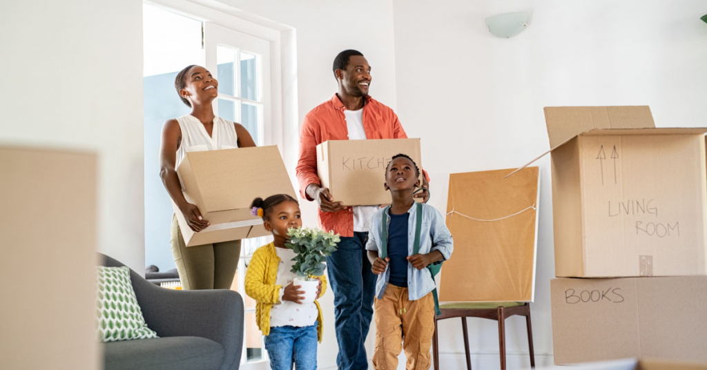 Beautiful african american family with two children carrying boxes in a new home